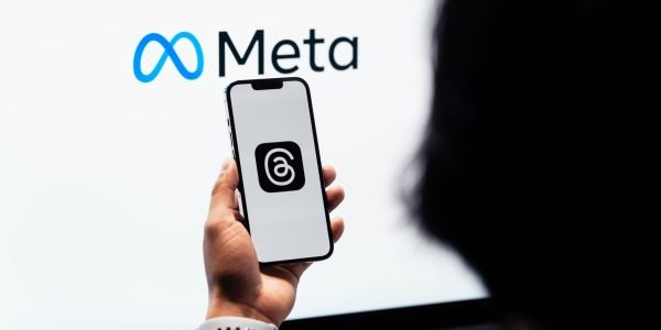 Hands holding smartphone with Meta Threads logo on screen, Meta branding in background.